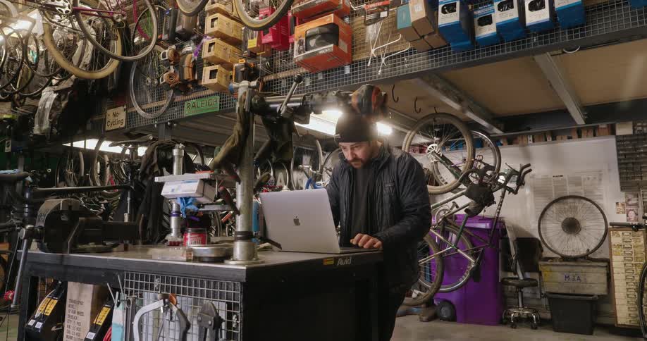 A man is typing on a laptop in the bike shop