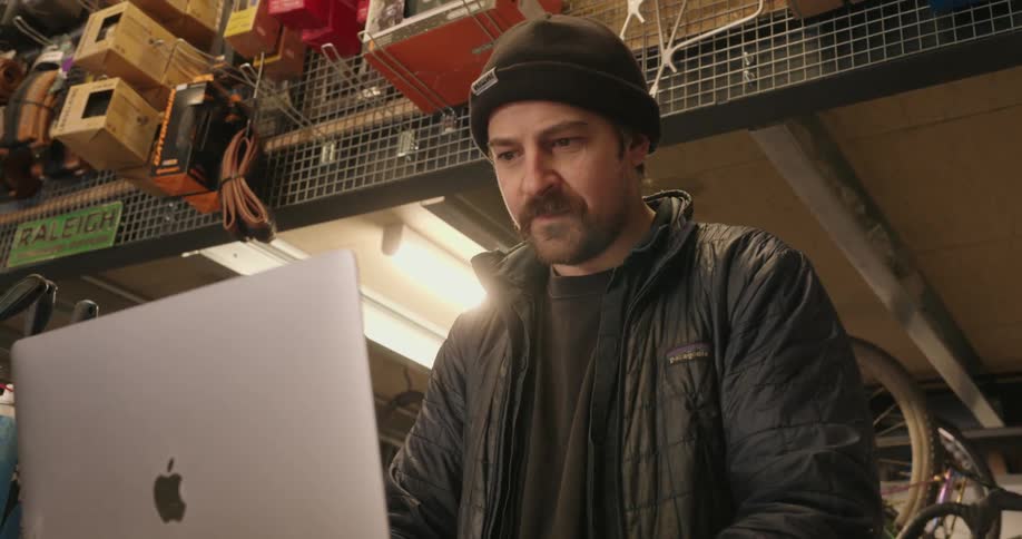 A man stands in a bike shop and looks at a laptop screen
