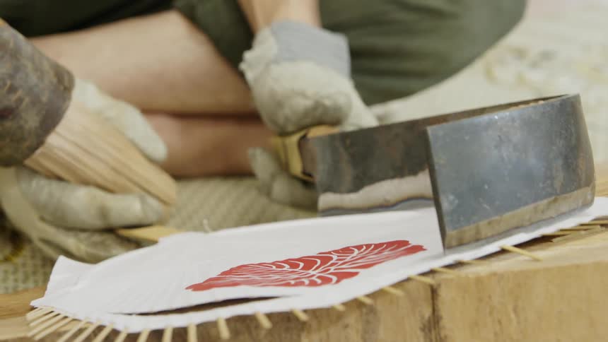 A person uses tools and a stencil pattern on a piece of wood