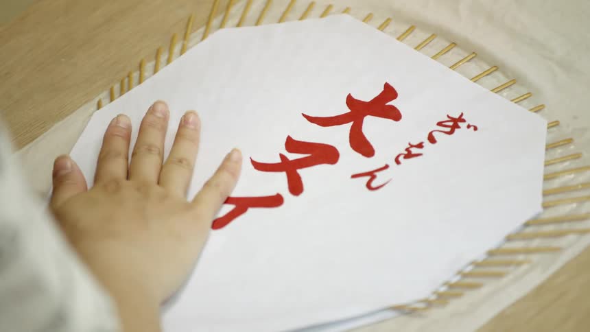 A woman assembles a hand fan with chinese characters