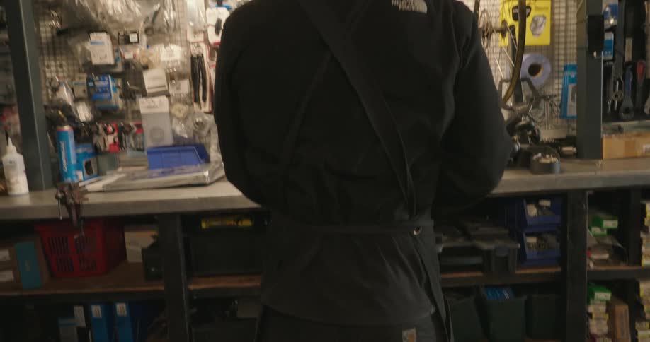 A man ties on an apron in the bike shop