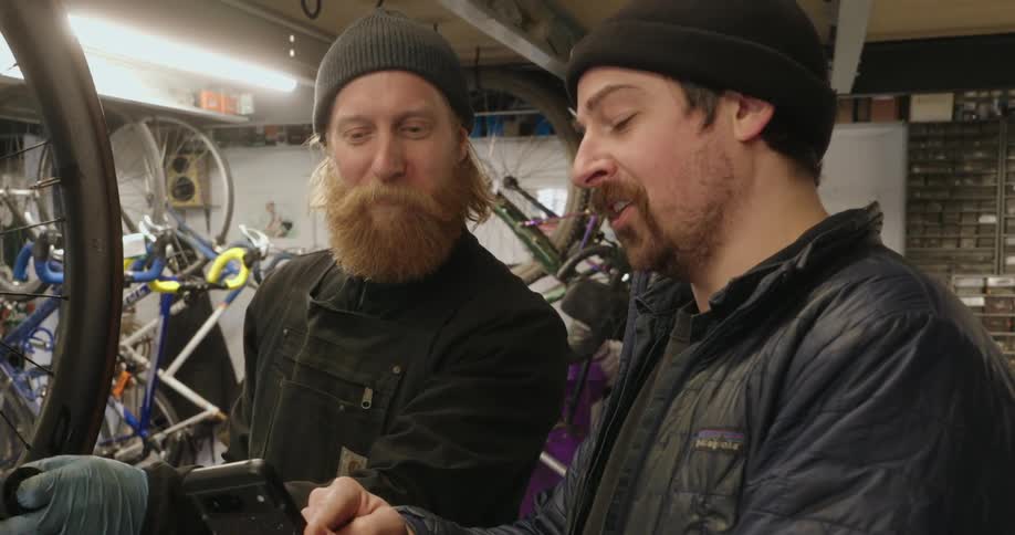 Man in a bicycle shop uses his smartphone to illustrate a point during a discussion
