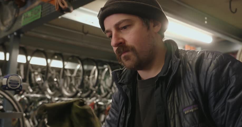 A man working in a bicycle shop cleans a small metal part with a rag