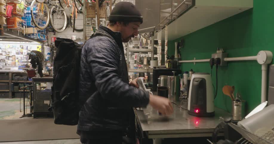 A man standing in a bicycle shop pours coffee beans into an electric grinder