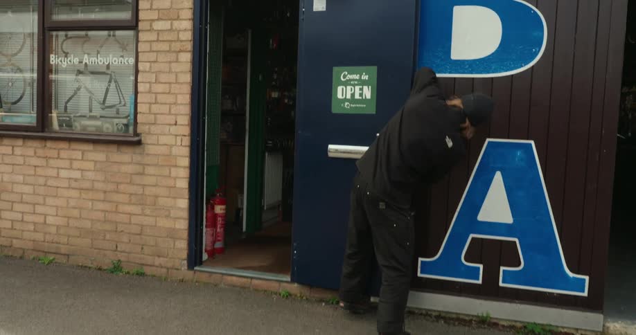 A man opens up the shop and puts the open sign on the door