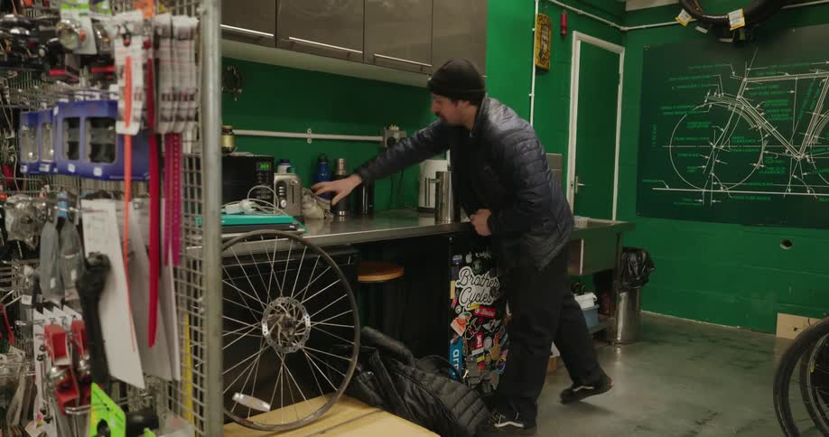 A worker puts down his bag in the bike shop and puts mugs on the counter