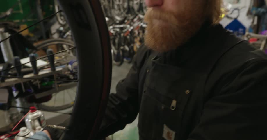 A white man with a thick beard fixing a bike tire inside a bike shop