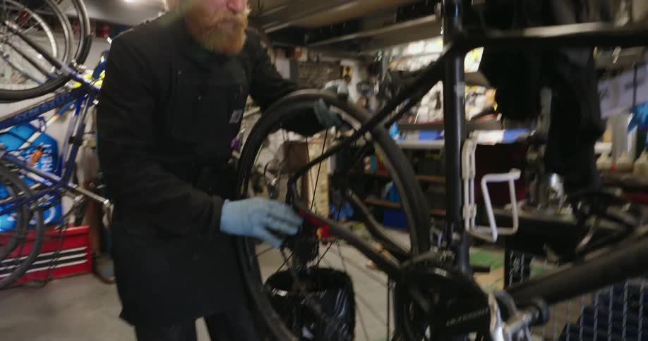 A cluttered workshop with a person repairing a bicycle surrounded by scattered tools and spare parts