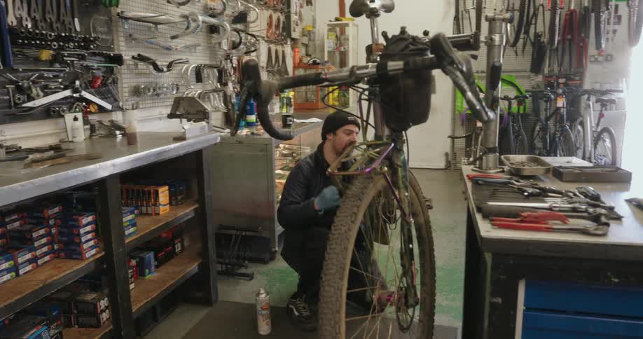 Two mechanics work on bicycles in a cluttered repair shop