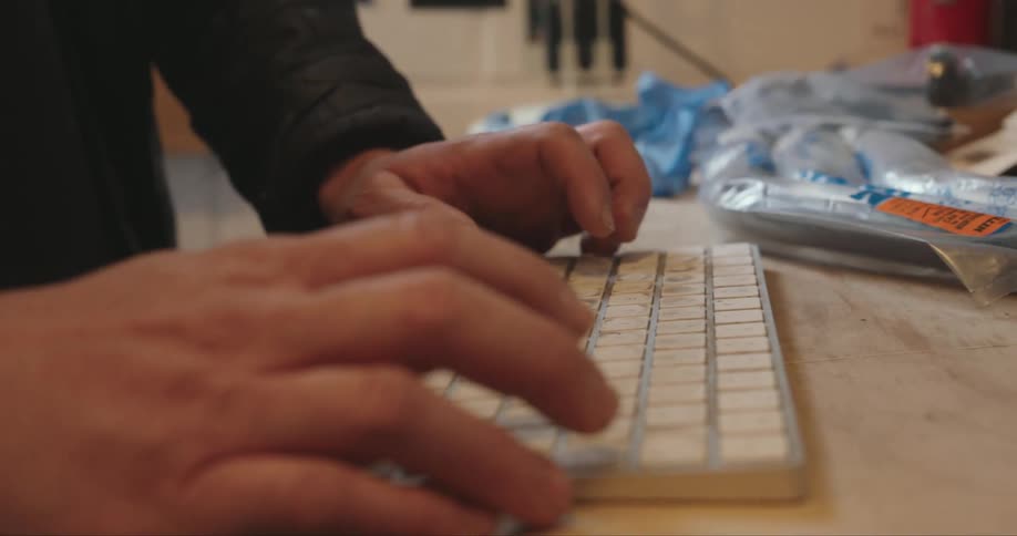 A person types on a white keyboard set on a wooden desk cluttered with tools and other items