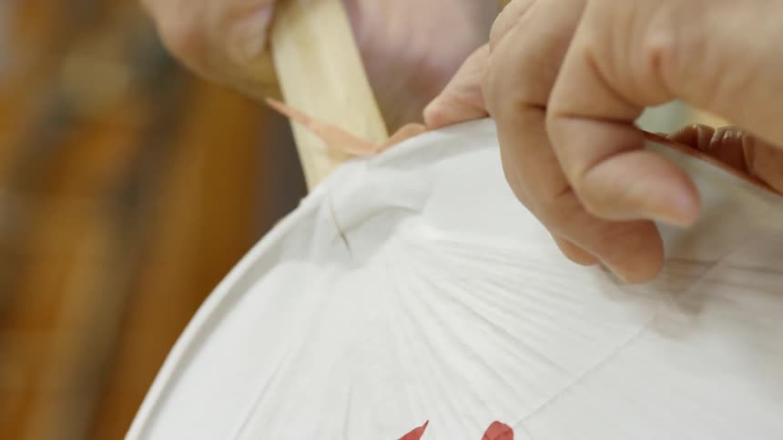 A person applies a border to a fan with chinese characters