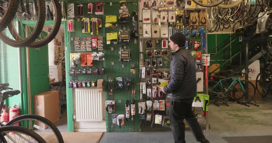 A man in the black jacket and cap is walking up to a wall of objects and putting some objects in order
