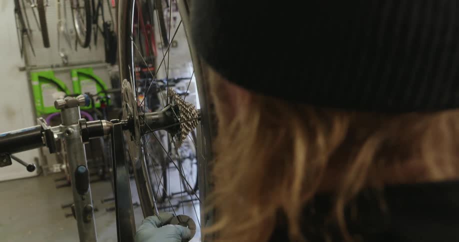A closeup overtheshoulder view shows a mechanics gloved hands meticulously adjusting the spokes on a bicycle wheel mounted in a repair stand