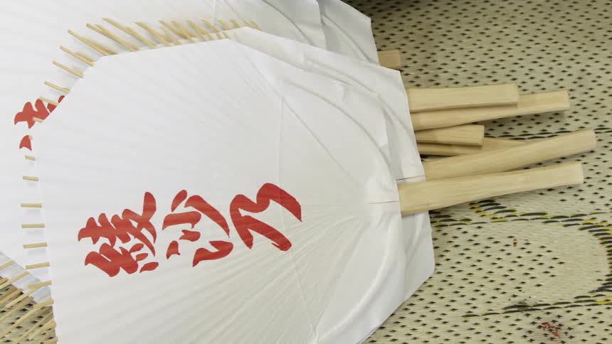 A person wearing a work glove picks up an asian paper fan