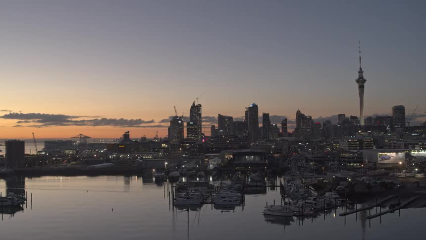The auckland city skyline and harbor are seen peacefully reflecting in the water at twilight