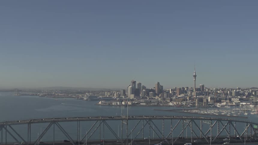 Traffic crosses a bridge across an expanse of water from the waterfront city skyline on a hazy day