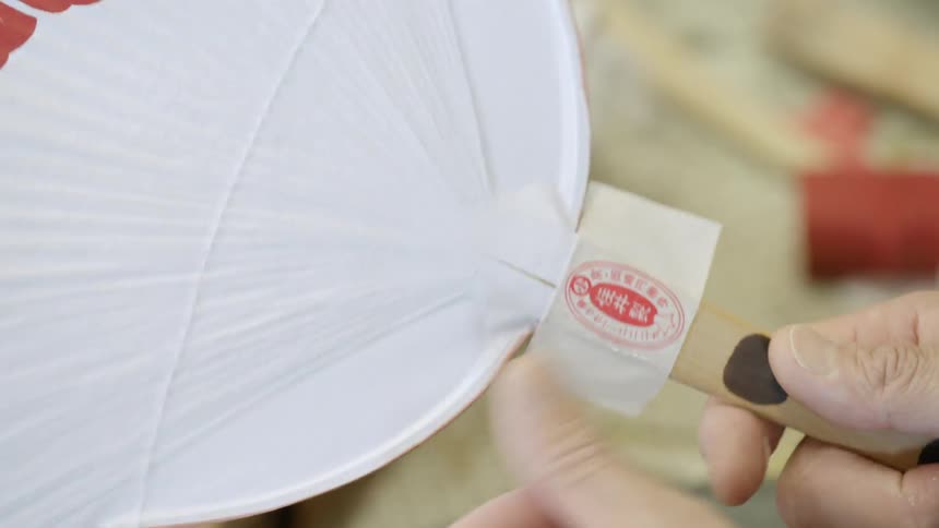 Person puts a sticker around a paper fan handle