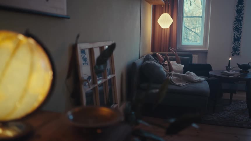 A woman is using a cell phone while laying on the couch