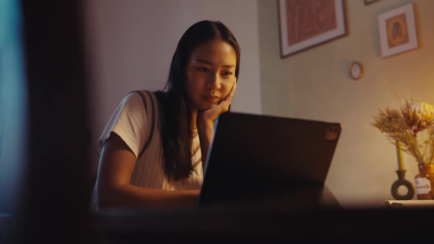 Woman sitting in a lowlit room and interacting with a laptop in front of her