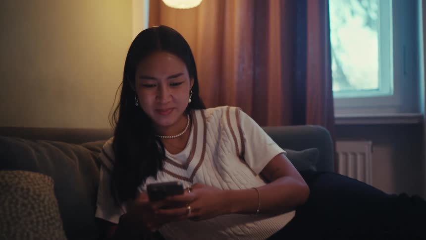 Woman leaning on a sofa smiles while using her smartphone during the daytime