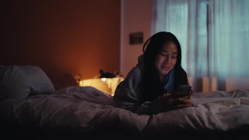 Young woman rolling around in bed and interacting with a smartphone