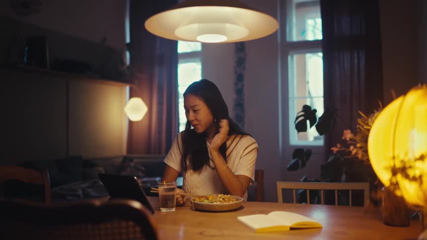 Woman sitting at a table during meantime waves while making a video call during the daytime