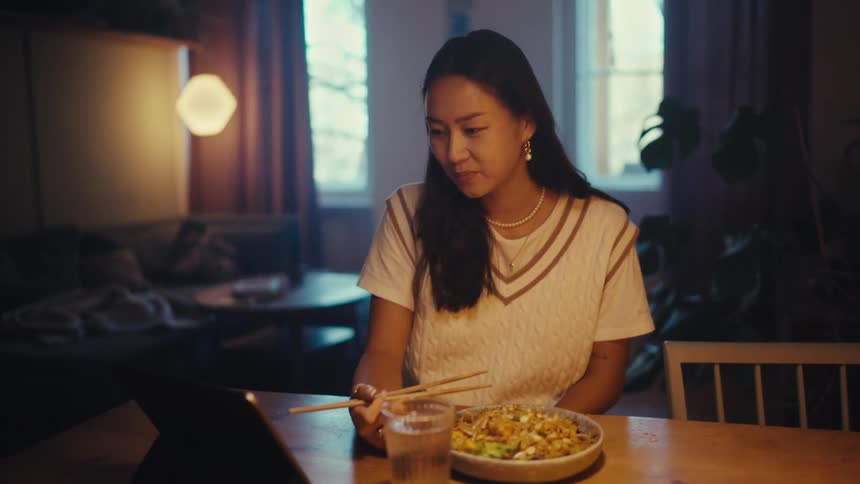 Woman converses during a video call on her tablet while sitting at her dining table with her food