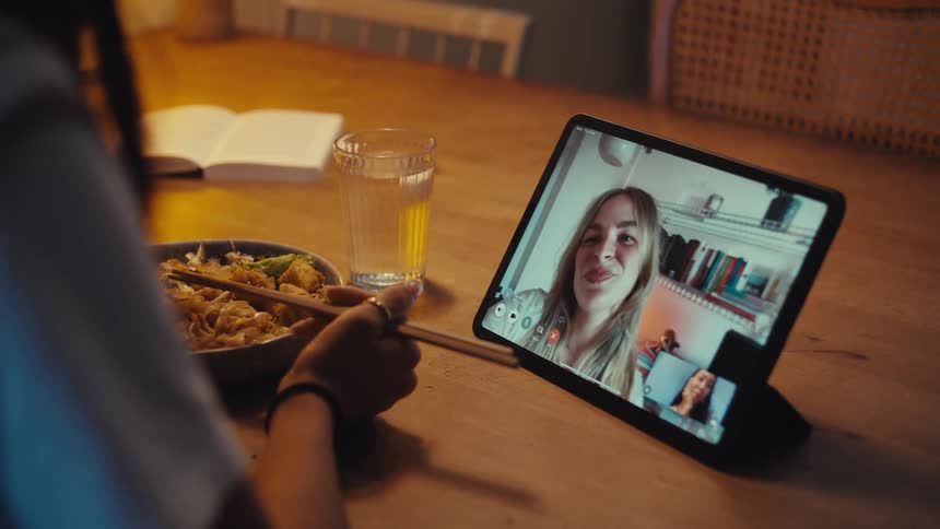Woman shares a video call with a friend during her mealtime at home