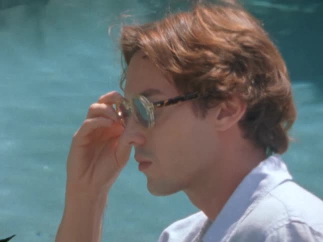 A person stands near a swimming pool wearing a light blue shirt
