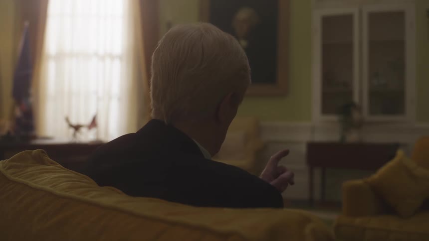 The back of the neck of a grayhaired man who is sitting on the couch pointing his index finger forward