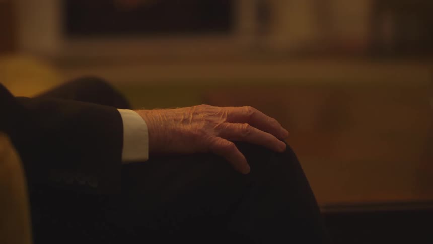 An older man pats his knee and holds his hand out before he starts to point
