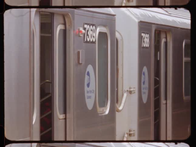 A new york city subway train repeatedly opens and closes its doors at an outdoor station