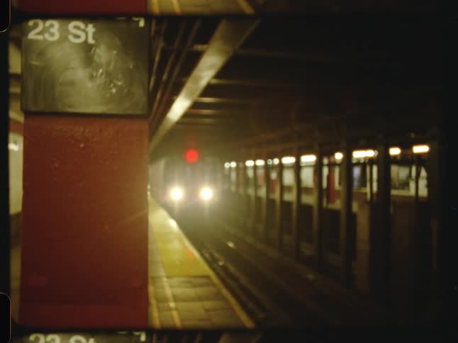 A trains headlights cut through the darkness as it approaches the platform of the 23 st subway station in olderlooking footage