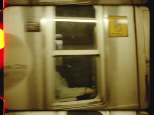 A new york city subway train pulls into a station captured with the grainy aesthetic of vintage film