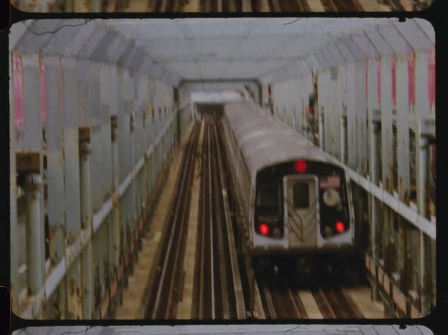 Public train travels along an elevated railway paralleling a street during the daytime