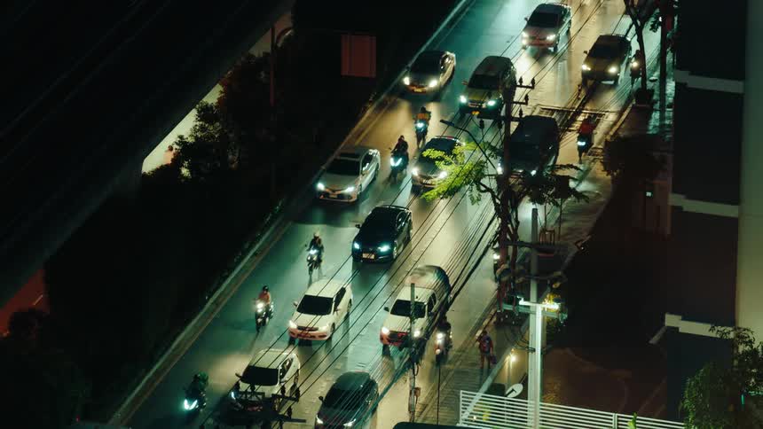 An aerial view of a series of cars and motorcycles moving side by side on a busy city road during nighttime traffic