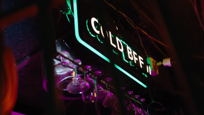 A series of glasses hanging in a glass rack inside a pub with a sign above that says cold bff