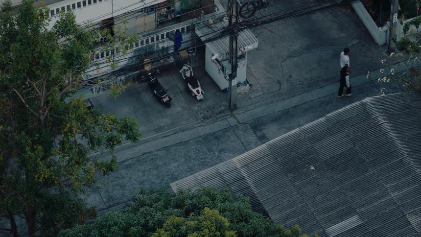 Two people walk down a narrow urban street past parked motorcycles