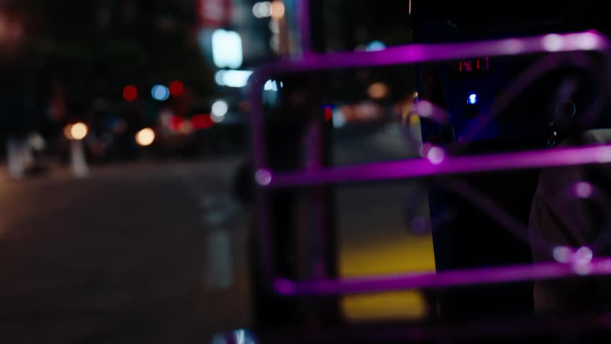 A car with a purple cagelooking bumper drives through downtown at night