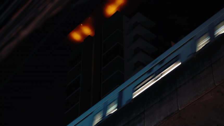 A lit train speeds past a dark building at night