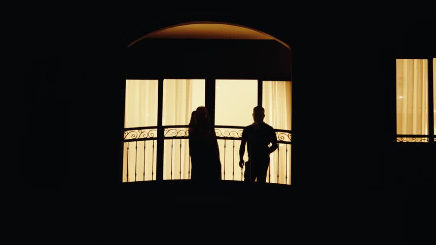 A woman and a man in a lobby next to a window both smoking cigarettes as the environment remains dim despite daylight reflecting through the window