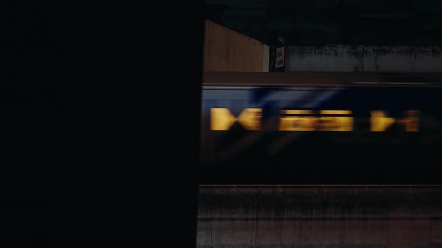 A train with lit windows speeds under a dark bridge