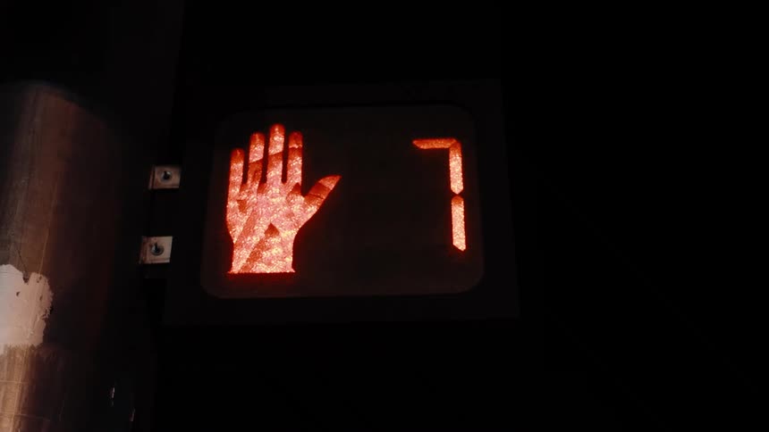 A digital pedestrian crossing signal counts down from 15 to 0 in glowing orange numbers against a dark background ending with a red hand symbol