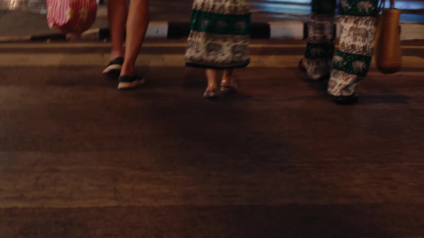 A couple walking with their child as they cross a city road at night both the man and the woman are holding handbags while the child in the middle holds onto both parents arms