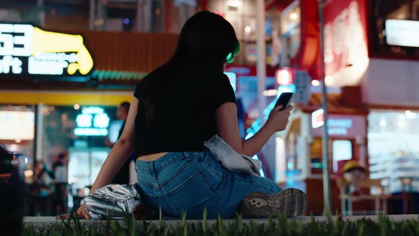 A woman sits on a concrete ledge while scrolling on her phone