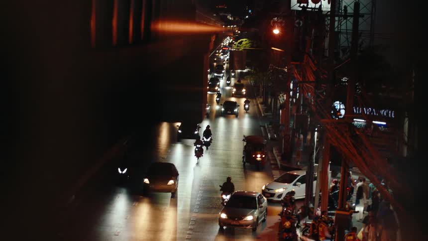 A street with 3 lanes and lots of cars and motorbikes moving down the road with incoming traffic turning onto the road