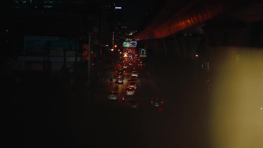 A series of cars caught in traffic moving slowly side by side on a busy freeway with road signs reflecting the light from the cars due to nighttime