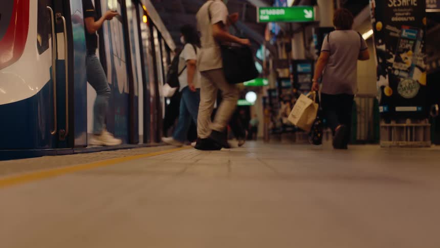 Commuters exit a train onto a busy platform as its doors open at an elevated station