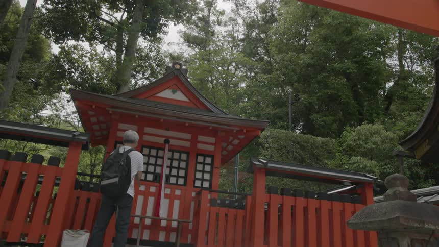 A man stands at a structure with asian architecture as trees tower overhead
