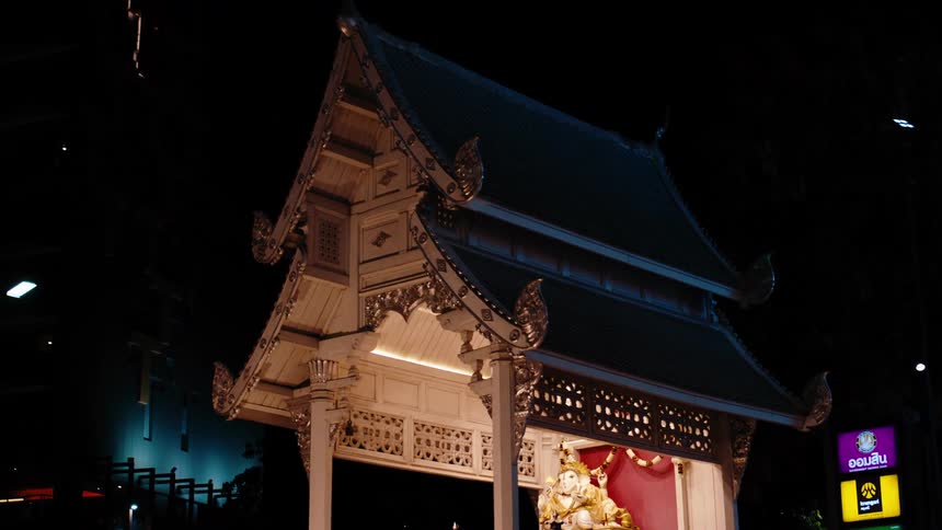 Brightly lit shrine containing an elaborate gold accented statue contrasts with the dark of the night